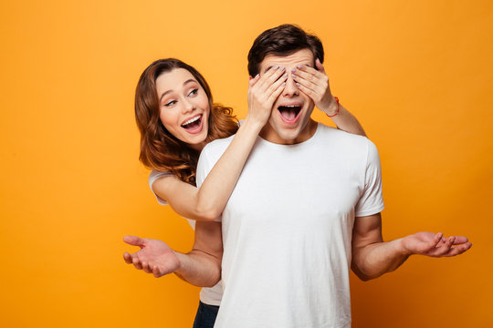 Happy brunette woman standing behind man and covering his eyes