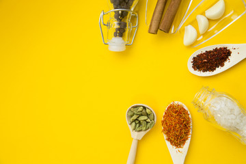 Plastic spoons with dry spices and fresh herbs on a yellow background with copy space, top view, close up