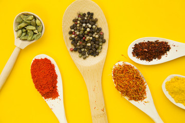 Wooden and plastic spoons with dry spices and fresh herbs on a yellow background with copy space, top view, close up