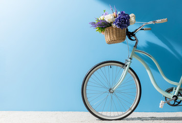 front wheel of bicycle with flowers in basket in front of blue wall - obrazy, fototapety, plakaty