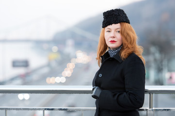Aged woman in black coat on bridge. Urban girl in black coat with rouge hair. Portrait of urban woman. Autumn likes rouge women