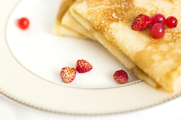 Тонкие блины, свернутые треугольниками со свежими ягодами красной смородины и земляники на белой фарфоровой тарелке