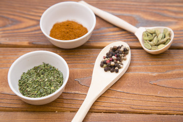 Plastic spoons and cups with dry spices and fresh herbs on a wooden rough boards background, top view, close up