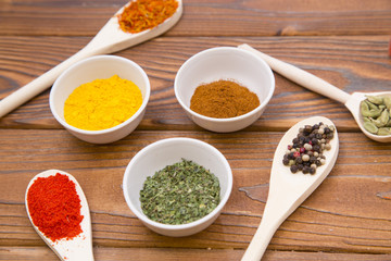 Plastic spoons and cups with dry spices and fresh herbs on a wooden rough boards background, top view, close up