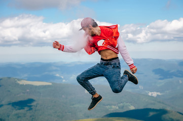 Strange bizarre unusual happy male person jumping in sky. Traveler man smoking electronic cigarette on top of mountain. Young rebel boy portrait flying in clouds. Leisure activity outdoor. Scenic view