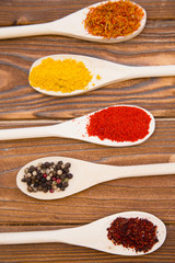 Plastic spoons with dry spices and fresh herbs on a wooden rough boards background, top view, close up