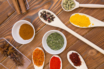 Plastic spoons and cups with dry spices and fresh herbs on a wooden rough boards background, top view, close up