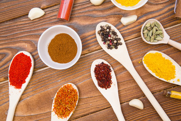 Plastic spoons and cups with dry spices and fresh herbs on a wooden rough boards background, top view, close up