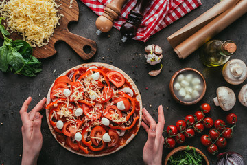 cropped shot of woman holding unbaked pizza on concrete table