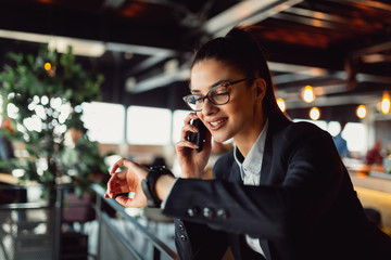 Shot of a happy young businesswoman talking with somebody on her mobile phone and checking the time.