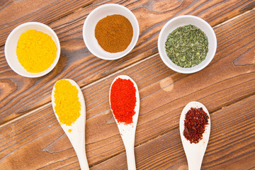 Plastic spoons and cups with dry spices and fresh herbs on a wooden rough boards background, top view, close up