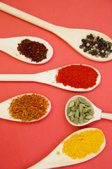 Plastic spoons with dry spices and fresh herbs on a rose background, top view, close up