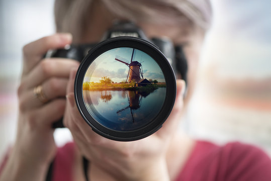Portrait of a young woman tourist standing with photo camera on the beautiful landscape background with old windmills in Netherlands
