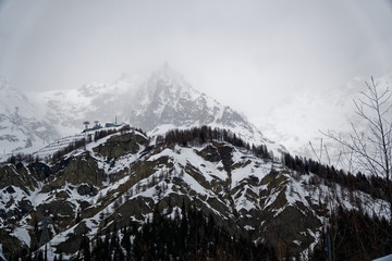 Mountains in the fog covered with snow and winter forest near Mont Blanc Alpes, Italy