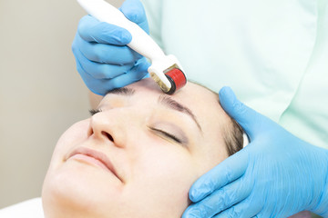 Naklejka premium The woman undergoes the procedure of medical micro needle therapy with a modern medical instrument derma roller 
