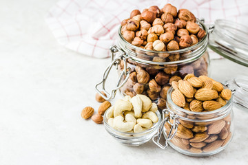 Nut mix in glass jars, walnuts, hazelnuts, almonds, cashew on white background. Selective focus, copy space.