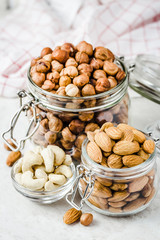 Nut mix in glass jars, walnuts, hazelnuts, almonds, cashew on white background. Selective focus, copy space.