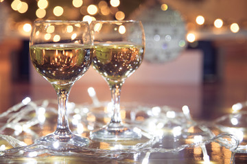 Tall wine glasses with bubbly drink for celebration toast wrapped in a Christmas light. Decorated christmas tree in the background. Holiday concept.