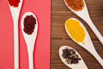 Plastic spoons with dry spices and fresh herbs on a wooden rough boards and rose background, top view, close up