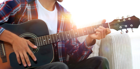 Handsome man playing on the guitar on the couch at home