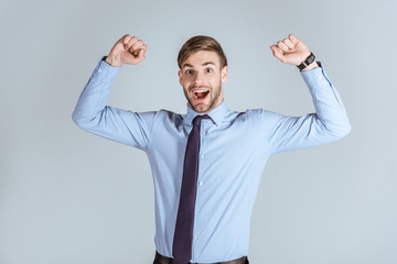 Young strong businessman raising arms up isolated on grey