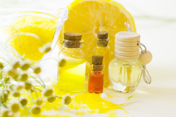Fruit aromatherapy concept with essential oil in glass bottles, a bowl of bath sea salt, flowers and lemon, white background, close up