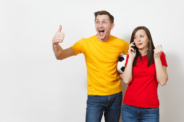 Fun engaged young man, indifferent woman talking on mobile phone, football fans cheer up support team with soccer ball isolated on white background. Sport, couple, family leisure, lifestyle concept.