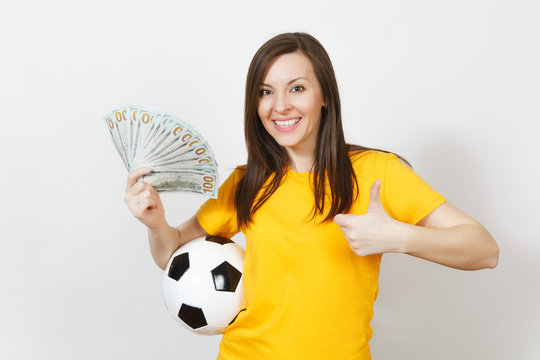 Young fun woman football fan or player in yellow uniform showing thumb up hold bundle cash dollars soccer ball isolated on white background. Sport, play football game, excitement lifestyle concept.