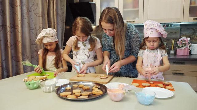 Mother helps her daughters to decorating the cookies with glaze.