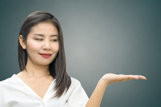 attractive Asian business woman hand showing or presenting something smiling over grey background with copy space 