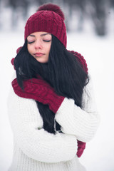 A sweet, tender and sensual young woman in a white sweater and a bright hat, scarf and mittens