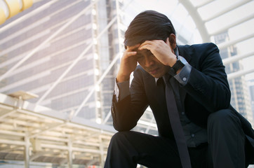 disappointed, sadness or stressed medium aged unemployed asian business man sitting on the walkway in the city after fired from job, business problem, unemployment, financial and investment concept