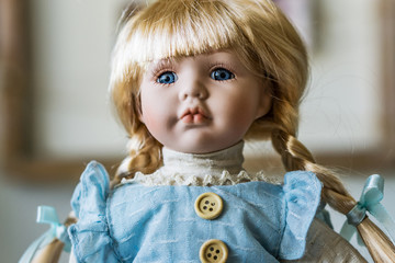 Close-up of beautiful porcelain doll with blond hair and blue eyes, sky blue vintage dress and leather shoes. Little princess games.