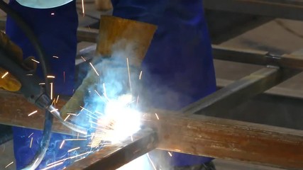 A man works with a welding machine. Welding steel structures in the factory. Beautiful sparks fly out - Powered by Adobe