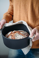 Male hands Rustic crusty bread boule in a cast iron pan