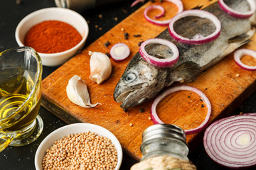 Fresh fish with herbs and spices on vintage cutting board on dark background