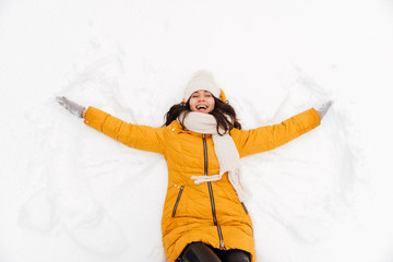 Happy playful lady lying on snow and making snow angel figure