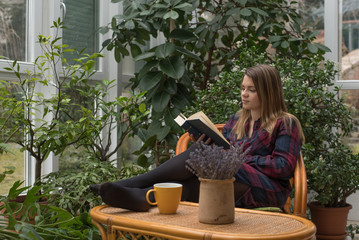 Beautiful young woman is is reading a book in winter garden