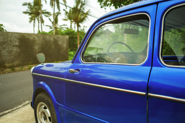 Fototapeta na wymiar Side view on retro blue car in tropical city. Palms are on background. Ready to travel.
