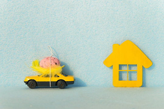 Yellow car with an egg on the roof and a house on a blue background. Easter concepts. Holiday for Easter. Travel to Easter holidays. Travel for the weekend.