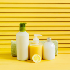 Towel and bottles with shower gel, shampoo and milk. Yellow background.