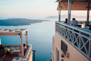 View of the pink-blue sunset on the island of Santorini to the sea, the sky and islands with people sitting back in a cafe in the foreground, with a large empty space, horizontal