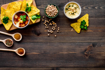 Serve hummus. Bowl with dish near pieces of crispbread on dark wooden background top view copy space