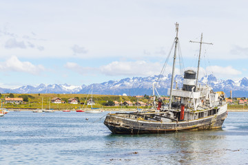 Fototapeta premium Old boat in Beagle channel with mountains and houses in Ushuaia