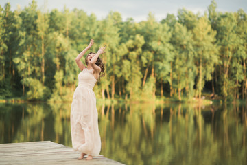 Gorgeous bride in elegant dress holding bouquet posing near forest and lake