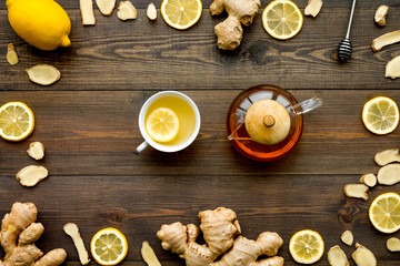 Tea for cure colds. Cup, teapot, ginger root and lemon on dark wooden background top view copy space