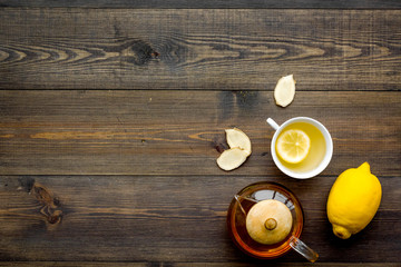 Tea for cure colds. Cup, teapot, ginger root and lemon on dark wooden background top view copy space