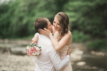 Beautifull wedding couple kissing and embracing near the shore of a mountain river with stones