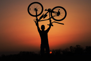 Silhouette of a guy holding his bicycle at sunset
