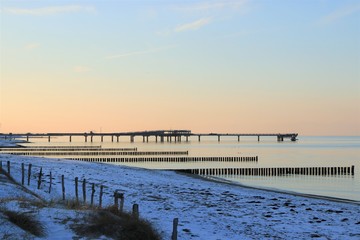 Fototapeta premium idyllischer Strand mit Buhnen und Seebrücke an der Ostsee im Winter mit Schnee, Konzept Winterlandschaft